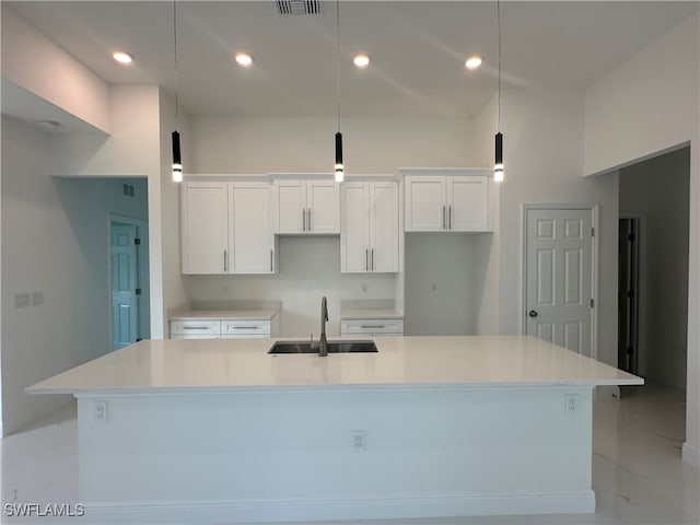 kitchen featuring a large island with sink, sink, white cabinets, and decorative light fixtures