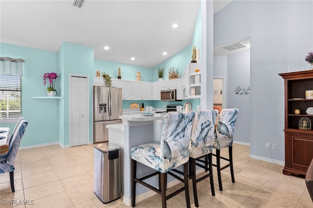 kitchen featuring stainless steel appliances, white cabinetry, a kitchen bar, light tile patterned floors, and kitchen peninsula