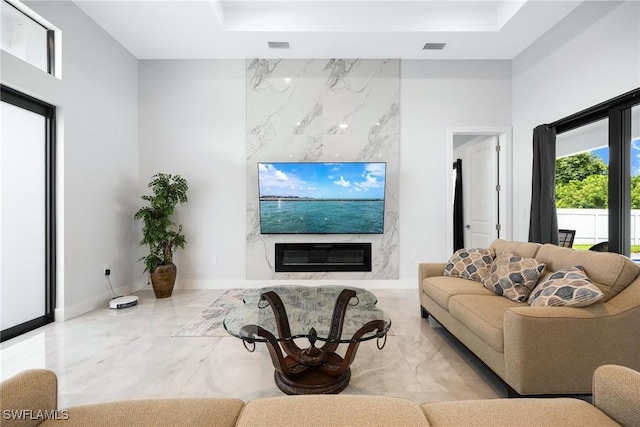 living area with a tray ceiling, marble finish floor, visible vents, a high ceiling, and a high end fireplace