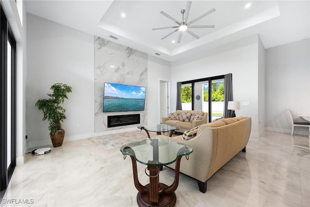 living area featuring a tray ceiling, marble finish floor, recessed lighting, a premium fireplace, and baseboards