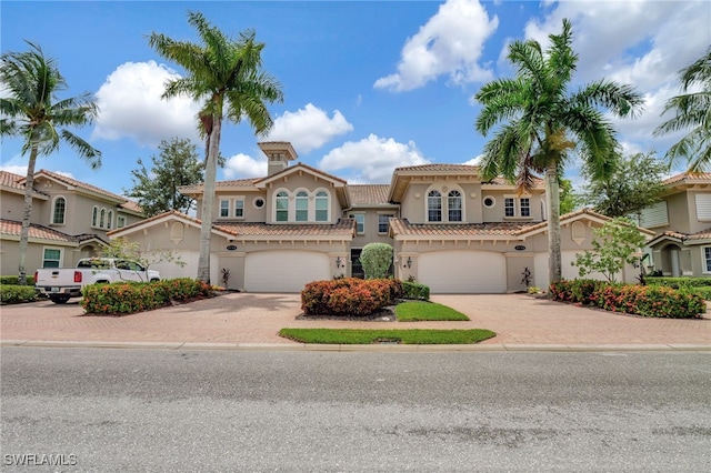 mediterranean / spanish-style home with an attached garage, a tile roof, decorative driveway, and stucco siding