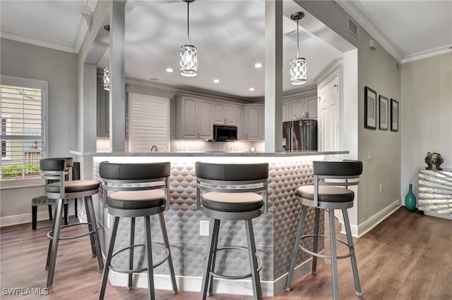 kitchen with gray cabinetry, a kitchen bar, stainless steel fridge, and hanging light fixtures