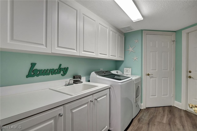 clothes washing area featuring cabinet space, visible vents, a textured ceiling, washing machine and dryer, and a sink