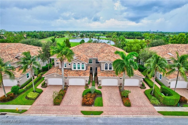 view of front of home featuring decorative driveway, a tile roof, stucco siding, a water view, and a garage