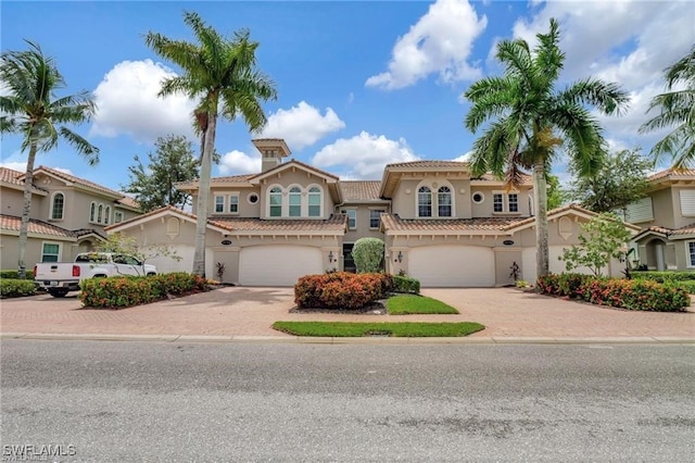 mediterranean / spanish-style home with a garage, a tiled roof, decorative driveway, and stucco siding