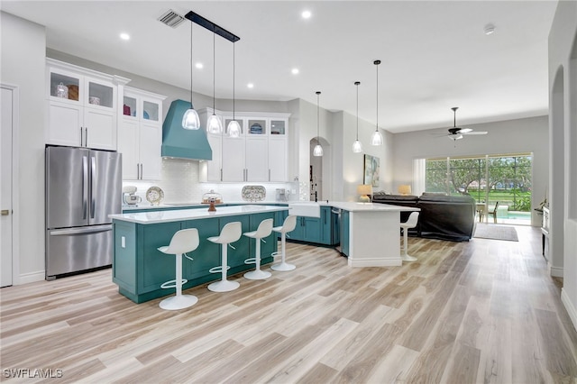 kitchen with custom range hood, light hardwood / wood-style flooring, stainless steel refrigerator, and a breakfast bar