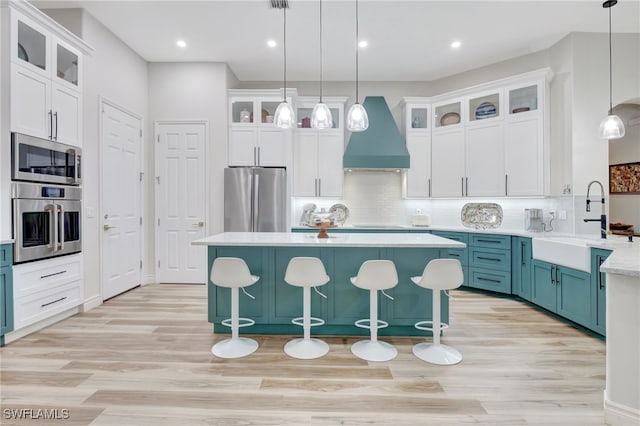 kitchen featuring backsplash, decorative light fixtures, premium range hood, appliances with stainless steel finishes, and light hardwood / wood-style floors