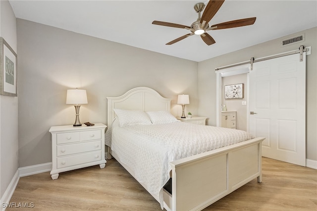 bedroom featuring light wood finished floors, visible vents, ensuite bathroom, a barn door, and baseboards