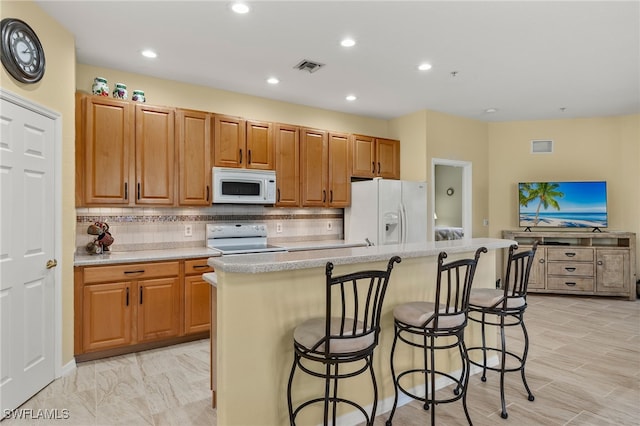 kitchen with a breakfast bar area, a center island with sink, backsplash, and white appliances