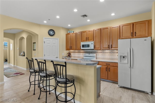 kitchen featuring tasteful backsplash, a kitchen bar, white appliances, and a kitchen island