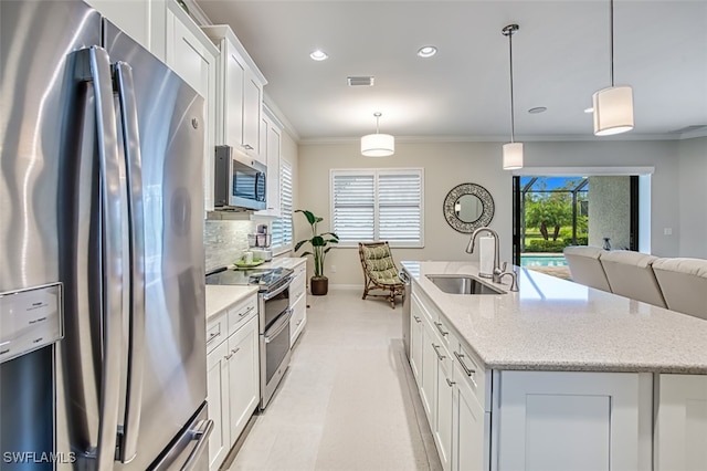 kitchen featuring appliances with stainless steel finishes, sink, white cabinetry, hanging light fixtures, and an island with sink