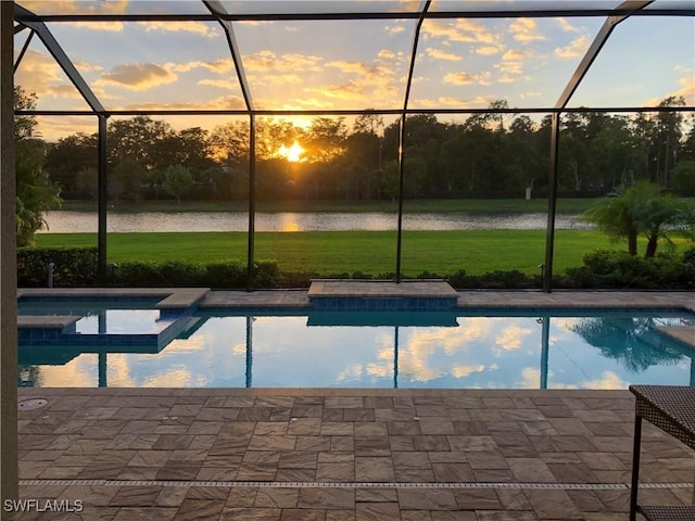 pool at dusk featuring a yard, a water view, and a lanai