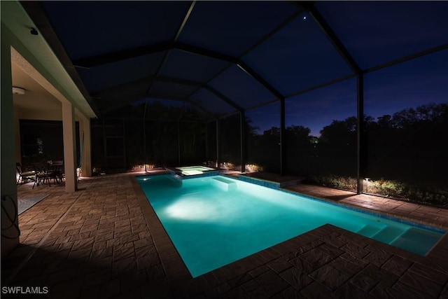 pool at night featuring an in ground hot tub, glass enclosure, and a patio area