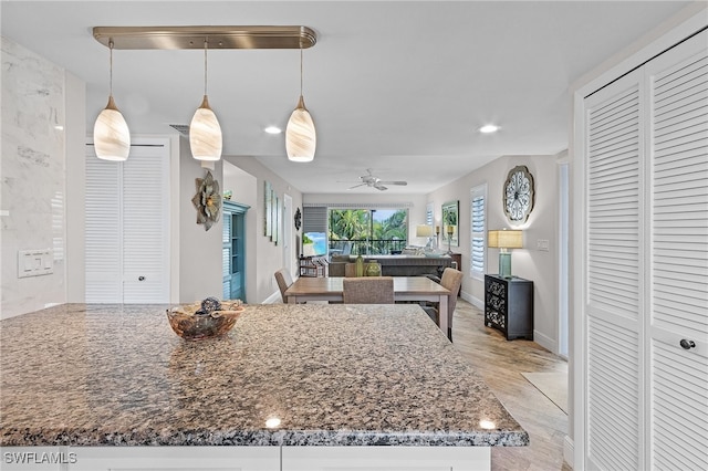 kitchen featuring light wood-type flooring, hanging light fixtures, ceiling fan, and stone counters