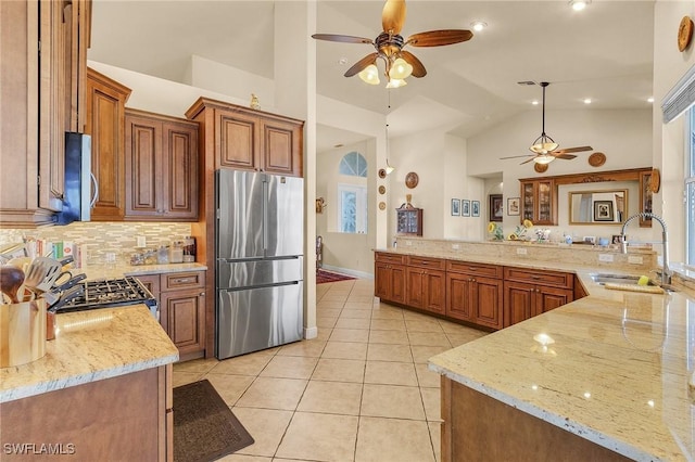 kitchen featuring pendant lighting, freestanding refrigerator, a sink, light stone countertops, and a peninsula