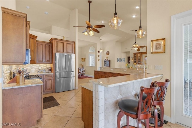 kitchen featuring brown cabinetry, a breakfast bar, decorative light fixtures, a peninsula, and freestanding refrigerator