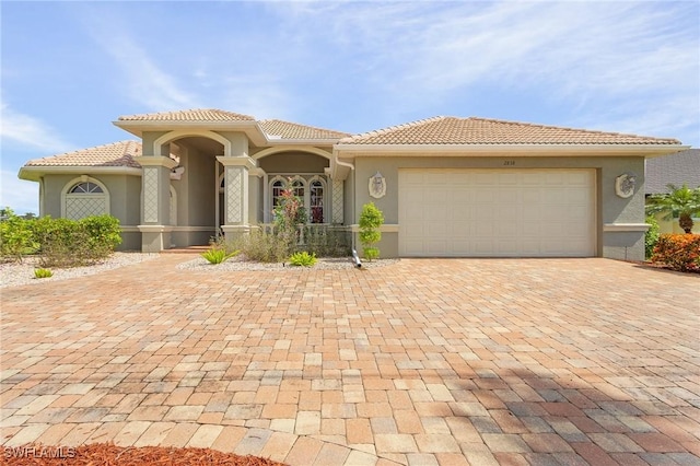 mediterranean / spanish-style house with a garage, decorative driveway, a tile roof, and stucco siding