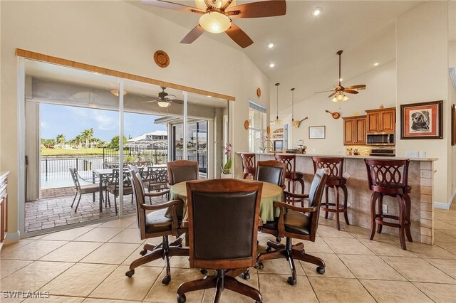 dining room featuring light tile patterned floors, high vaulted ceiling, a water view, and a ceiling fan