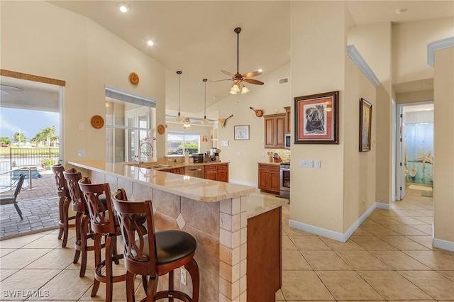 kitchen with a breakfast bar, brown cabinets, decorative light fixtures, a peninsula, and a sink