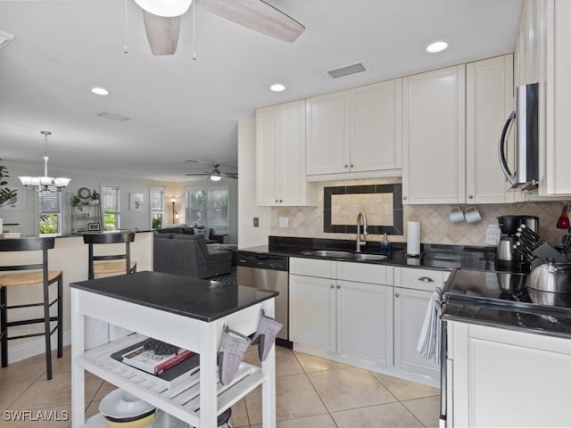 kitchen with appliances with stainless steel finishes, dark countertops, a sink, ceiling fan with notable chandelier, and white cabinetry
