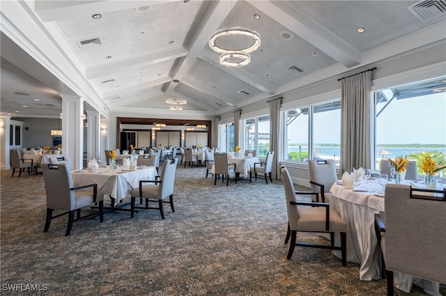 dining room with a chandelier, lofted ceiling with beams, a water view, carpet flooring, and decorative columns