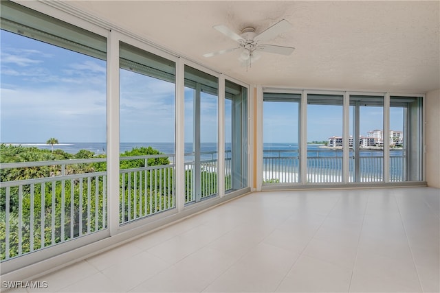 unfurnished sunroom with a wealth of natural light, ceiling fan, and a water view