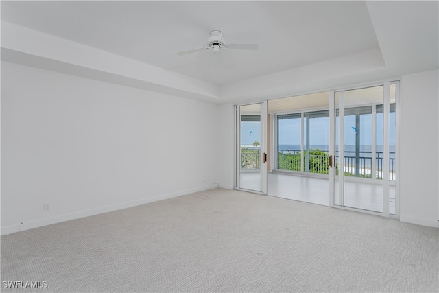 spare room featuring ceiling fan, a tray ceiling, a water view, and carpet flooring