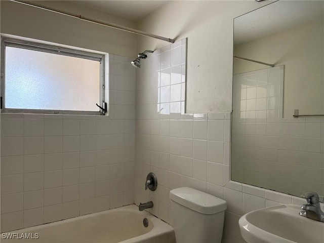 full bathroom featuring tiled shower / bath combo, toilet, sink, and tile walls