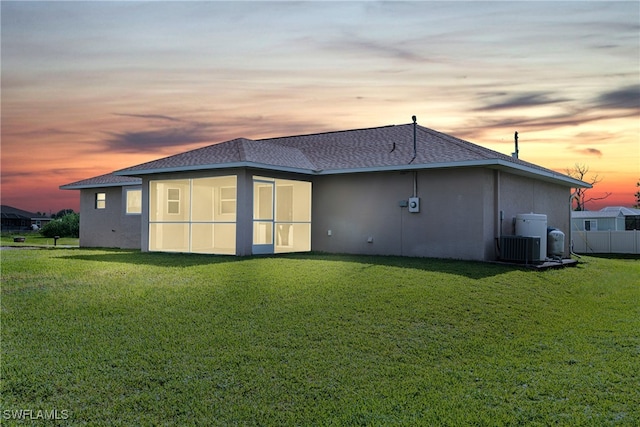 back house at dusk with cooling unit and a lawn