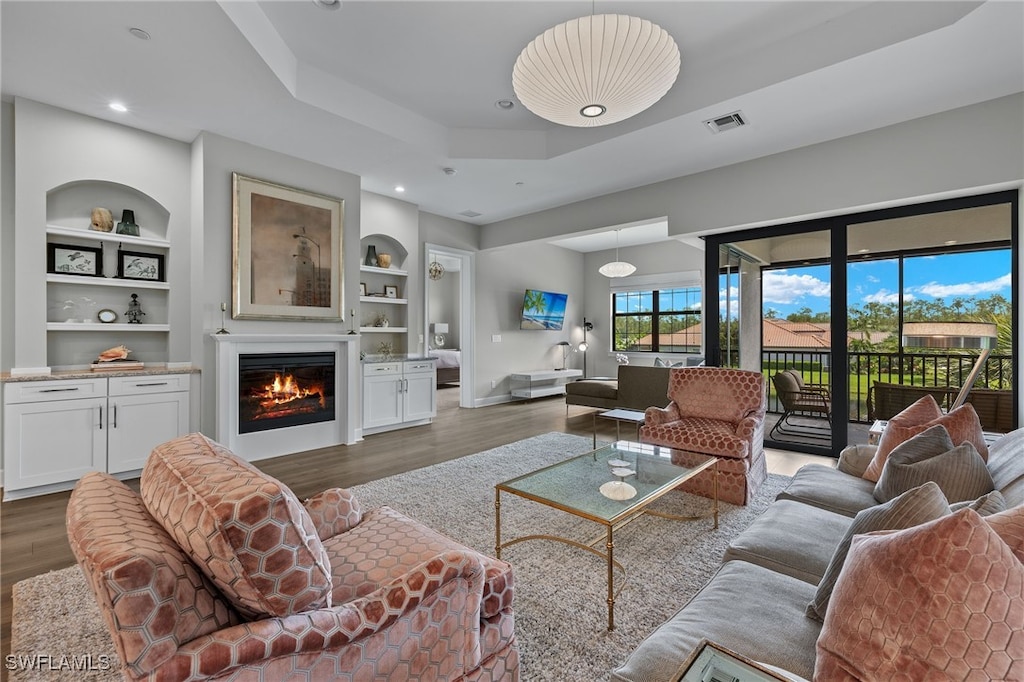 living room with built in shelves, dark hardwood / wood-style floors, and a raised ceiling