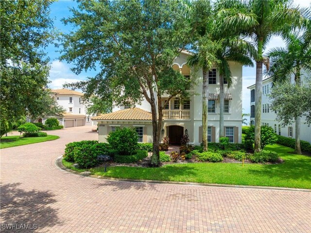 mediterranean / spanish home featuring a garage, a tiled roof, decorative driveway, stucco siding, and a front yard