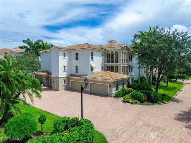 mediterranean / spanish home featuring a garage, decorative driveway, a tiled roof, and stucco siding