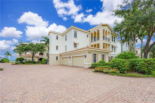 mediterranean / spanish-style home featuring a garage, a tiled roof, decorative driveway, and stucco siding