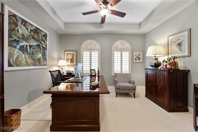 office featuring ceiling fan, a tray ceiling, light carpet, and baseboards