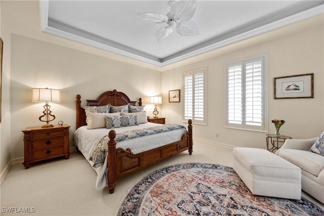 bedroom featuring light carpet, a tray ceiling, a ceiling fan, and baseboards