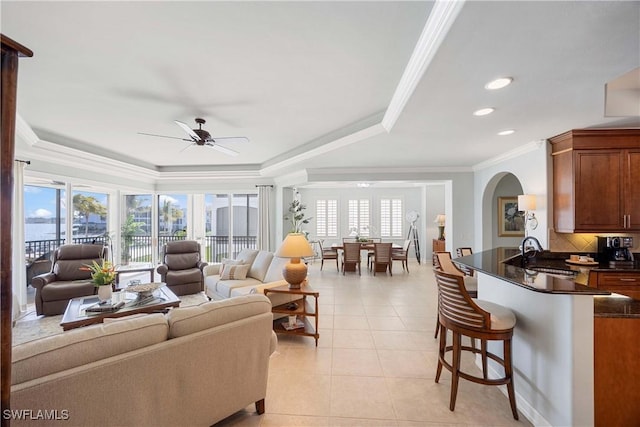 living room with arched walkways, a raised ceiling, a wealth of natural light, and light tile patterned flooring