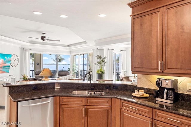 kitchen with dark stone counters, open floor plan, a tray ceiling, stainless steel dishwasher, and a sink