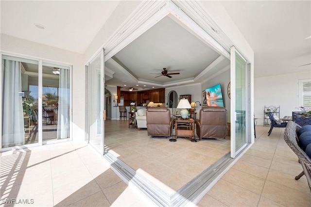 living area with light tile patterned floors, ceiling fan, and a raised ceiling