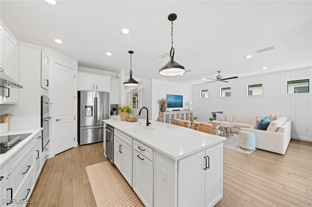 kitchen featuring white cabinets, a kitchen island with sink, stainless steel appliances, and light wood-type flooring