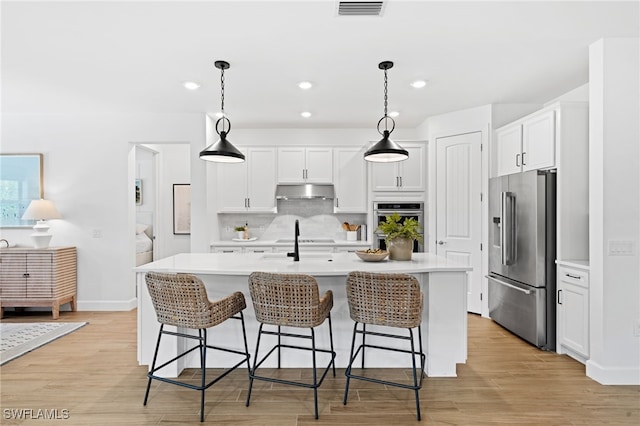 kitchen featuring pendant lighting, a center island with sink, appliances with stainless steel finishes, and light hardwood / wood-style flooring