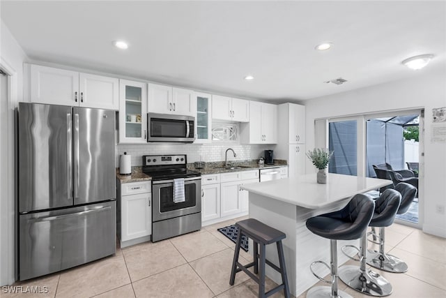 kitchen with a kitchen breakfast bar, decorative backsplash, white cabinetry, and stainless steel appliances