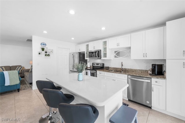 kitchen featuring a kitchen breakfast bar, sink, appliances with stainless steel finishes, light tile patterned flooring, and white cabinetry