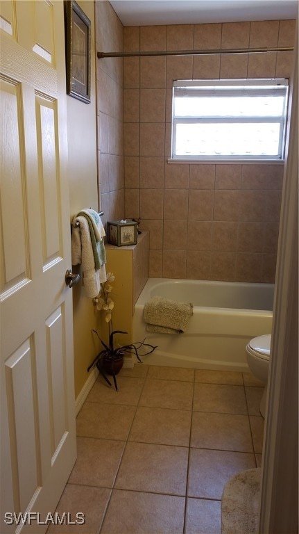 bathroom with tile patterned flooring, a healthy amount of sunlight, toilet, and tiled shower / bath