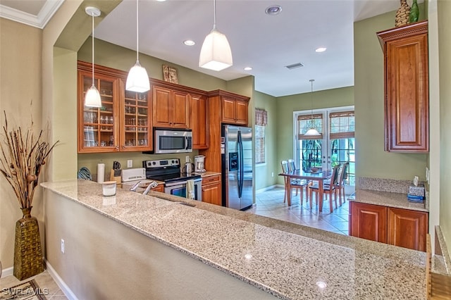 kitchen with appliances with stainless steel finishes, pendant lighting, light stone countertops, and ornamental molding