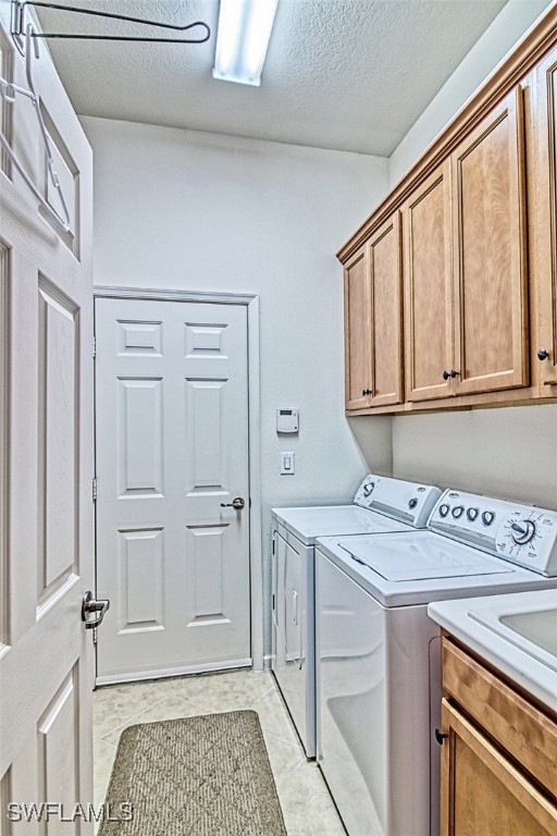 laundry area featuring light tile patterned flooring, cabinets, independent washer and dryer, and a textured ceiling