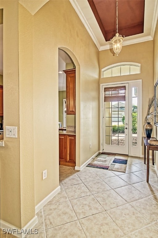 tiled entryway with crown molding, a raised ceiling, and an inviting chandelier