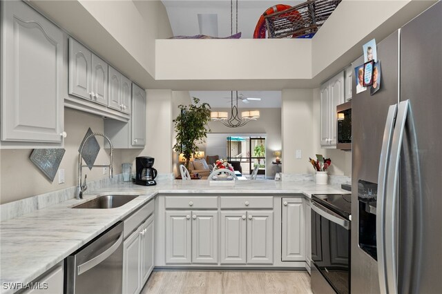 kitchen featuring sink, decorative light fixtures, stainless steel appliances, kitchen peninsula, and white cabinets