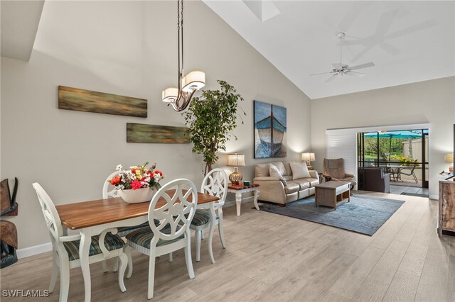 dining area with ceiling fan with notable chandelier, high vaulted ceiling, and light hardwood / wood-style flooring