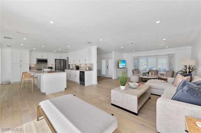 living room with sink, wine cooler, ornamental molding, and light hardwood / wood-style flooring