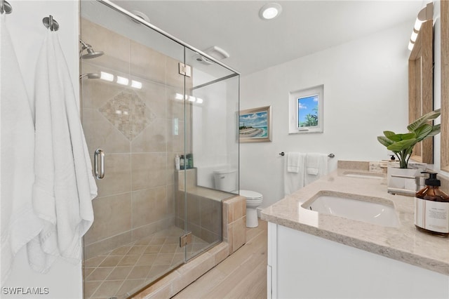 bathroom featuring vanity, a shower with shower door, hardwood / wood-style flooring, and toilet